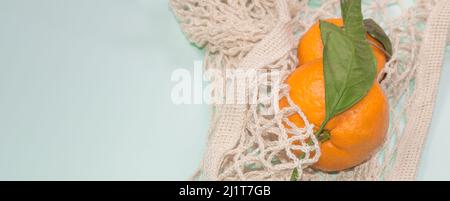 Blauer Bannerhintergrund mit Mandarinen in einem Saitenbeutel. Gesunder Lebensstil, Draufsicht, keine Verschwendung. Stockfoto