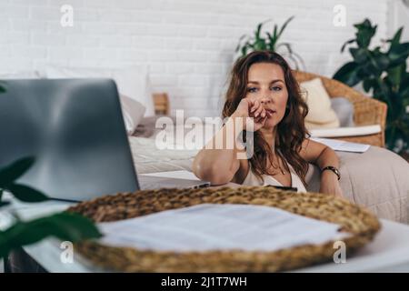 Porträt einer jungen Frau, die mit einem Laptop auf dem Boden sitzt und wegschaut Stockfoto