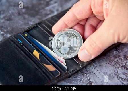 Krypto-Münze, XRP Ripple-Münze in Leder-Geldbörse auf Beton-Stil Hintergrund mit Clipping-Pfad. Hand mit einer Münze. Kryptowährung Geschäftskonzept. Hochwertige Fotos Stockfoto