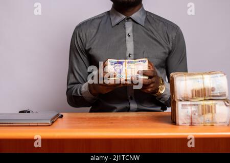 Ein glücklicher schwarzer junger Mann sitzt im Büro und hält viel Geld, Anlagekonzept Stockfoto