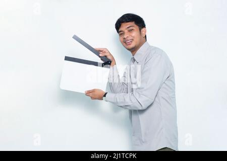 Junge lächelnde glücklich asiatischen Mann hält weißen Film machen Klappbrett isoliert auf weißem Hintergrund Stockfoto