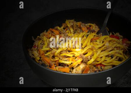 Geschredderte Ente unter Rühren mit Gewürzen und Gemüse in einer schwarzen Schüssel braten. Auf einem steinernen Hintergrund Stockfoto