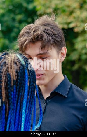 Ein junges heterosexuelles Paar spricht. Der Mann im schwarzen Hemd steht der Frau mit den langen blauen Dreadlocks gegenüber. Liebhaber vor Stockfoto