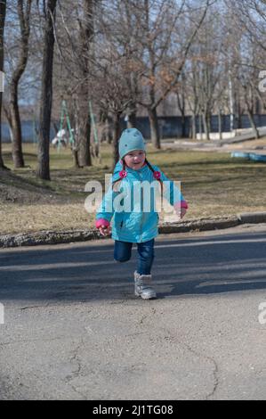 Porträt eines Kindes, das auf dem Bürgersteig läuft. Fünfjähriges Mädchen mit langen Zöpfen, die in die Kamera laufen. Kindheit. Draußen. Ein sonniger sp Stockfoto