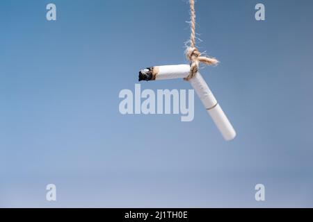 Welttag Der Tabakkontrolle. Die erloschene Zigarette hängt an einem Seil auf blauem Hintergrund. Speicherplatz kopieren. Das Konzept der Nikotinsucht. Stockfoto