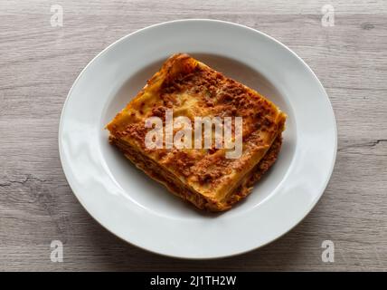 Italienische Fleischlasagne in einem weißen Gericht auf Holzhintergrund. Portion traditionelle Lasagne auf einem Teller. Stockfoto