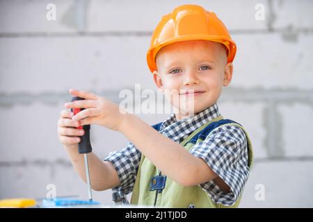 Kind im Helmbau, Schutzhelm. Kind als Bauarbeiter gekleidet. Portrait glücklich lächelnd kleiner Baumeister in Hardhats. Kleiner Baumeister im Helm. Stockfoto