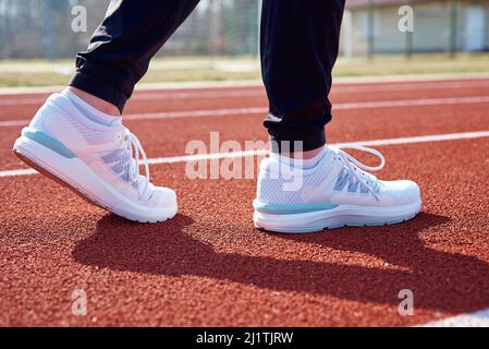 Männliche Läuferfüße mit weißen Sneakers auf der Stadionstrecke, Nahaufnahme. Sport-Sneaker zum Joggen. Fitness und gesundes Lifestyle-Konzept Stockfoto