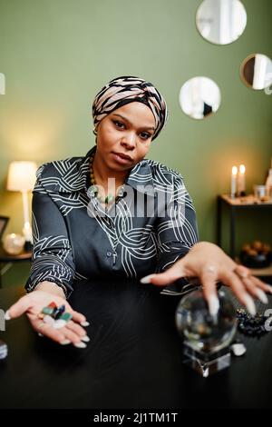Vertikales Porträt einer weiblichen Wahrsagerin, die mit Kristallkugel auf spirituelle Seance im Geschäft schaut Stockfoto