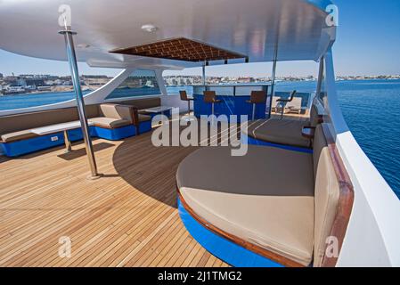 Sonnendeck aus Teakholz einer großen Luxus-Motoryacht mit Stühlen, Sofa-Tisch und tropischem Meerblick im Hintergrund Stockfoto