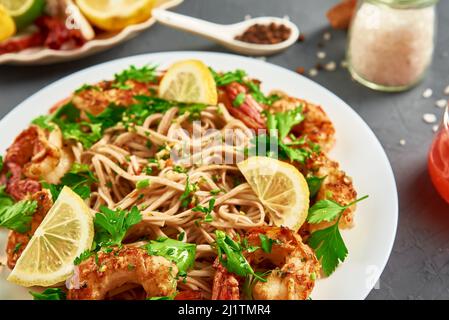 Nudeln mit Garnelen, Zitrone und frischer Petersilie auf weißem Teller unter Rühren braten, Soba mit Garnelen, asiatische Küche, Draufsicht Stockfoto