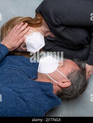Draufsicht auf eine Frau und einen Mann, der auf dem Boden liegt, kreuzten sich, liebkosen sich gegenseitig, tragen eine Gesichtsmaske Stockfoto