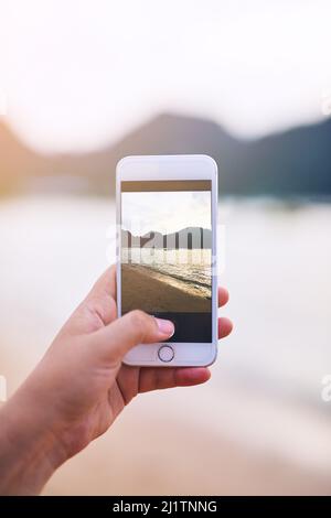 Den Moment festhalten. Ausgeschnittene Aufnahme einer jungen Frau, die am Strand fotografiert. Stockfoto