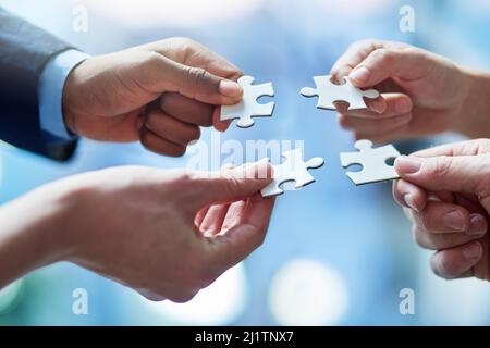 Das Rätsel im Team lösen. Eine kleine Aufnahme von Personen, die vier Puzzleteile zusammenfügen. Stockfoto