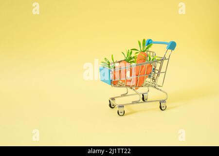 Einfacher kreatives Konzept des Einkaufskorbs voller Karotten für Kaninchen. Pastellgelber Hintergrund. Stockfoto