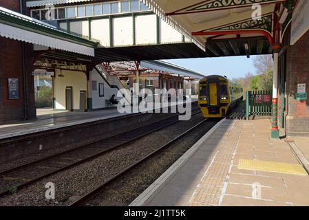 Passagiere, die auf dem Bahnsteig als Transport für Wales Class 158 'Express' DMU-Zug warten, kommen am Wrexham General Railway Station, März 2022 an Stockfoto