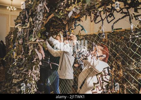 LVIV, UKRAINE - 17. März 2022: Freiwillige weden Tarnnetz für die ukrainischen Streitkräfte. Handgefertigtes Maskennetz aus naturfarbenen Teppichen Stockfoto