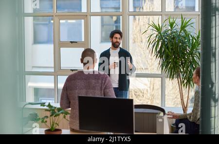 Ein junger Geschäftsmann, der sich mit Kollegen bei einem Kaffee in einem Büro unterhielt Stockfoto