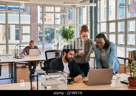 Eine Gruppe von konzentrierten Geschäftsleuten, die an einem Laptop arbeiten Stockfoto
