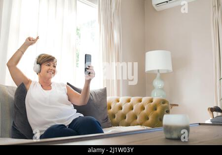 Dieser Song ist mein Favorit. Aufnahme einer reifen Frau, die ihr Smartphone benutzt, um ein Selfie zu machen, während sie Musik hört. Stockfoto