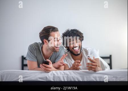 Fröhlich Gay paar nehmen Selfies im Bett Stockfoto