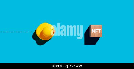 Toy Robber Duck bewegt sich zu einem Holzwürfel mit dem Akronym NFT für nicht fungible Token Kryptowährung. Business Finance-Konzept. Stockfoto