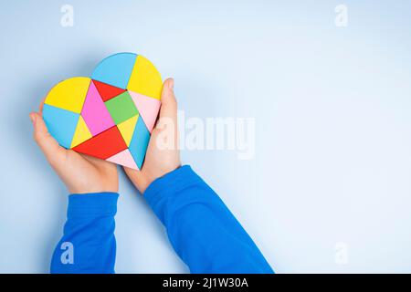 Kind Hände halten bunte Puzzle Herz auf hellblauem Hintergrund. Konzept des Welt-Autismus-Tages Stockfoto