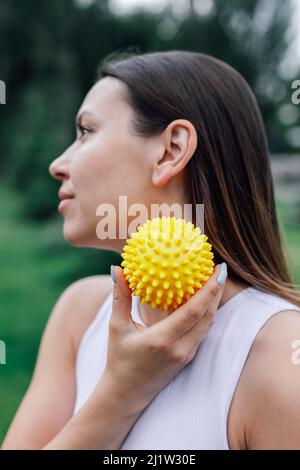 Spiky Gummi-Massage-Ball für die Erholung der Muskeln in den Händen der jungen Frau nach dem Training im Park Stockfoto