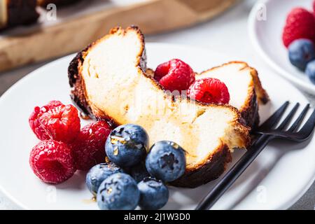 Eine Portion hausgemachter San Sebastian gebrannter Käsekuchen mit Beeren auf weißem Teller zum Frühstück, Nahaufnahme. Stockfoto