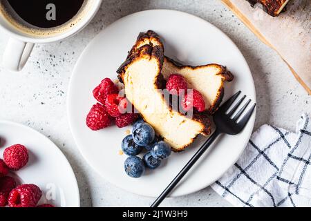 Flaches Lay von hausgemachtem San Sebastian gebranntem Käsekuchen mit Beeren auf weißem Teller zum Frühstück, Draufsicht. Stockfoto