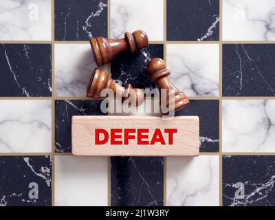 Schachfiguren auf dem Schachbrett mit dem Wort Niederlage auf einem Holzblock. Stockfoto