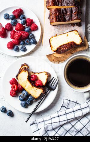 Flaches Lay von hausgemachtem San Sebastian gebranntem Käsekuchen mit Beeren auf weißem Teller zum Frühstück, Draufsicht. Stockfoto