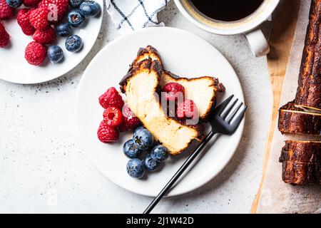 Flaches Lay von hausgemachtem San Sebastian gebranntem Käsekuchen mit Beeren auf weißem Teller zum Frühstück, Draufsicht. Stockfoto