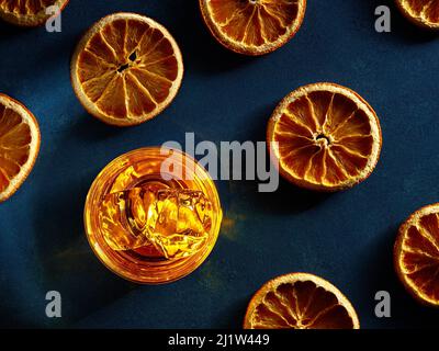 Ein Glas eleganter Whiskys mit Eis und getrockneten Orangen an einer Theke mit dunkler launischer Atmosphäre. Cocktailkonzept für harte Getränke. Stockfoto