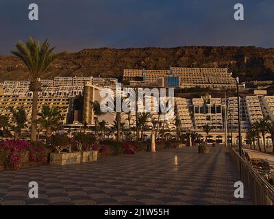 Blick auf die leere Strandpromenade des Ferienortes Taurito, südliches Gran Canaria, Kanarische Inseln, Spanien am Abend Sonnenlicht mit Palmen. Stockfoto