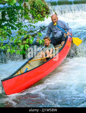 Vater und Sohn paddeln im Kanu ein Wehr hinunter Stockfoto