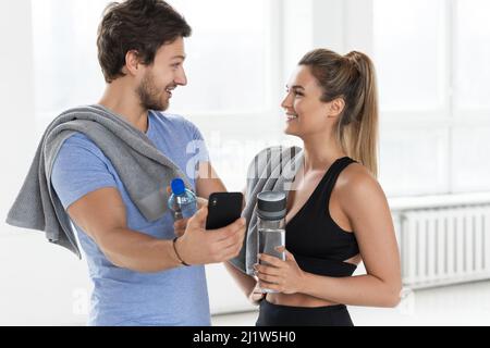 Mann und Frau während eines Trainings im Fitnessstudio. Kerl zeigt seinem Teamkollegen eine neue Fitnessanwendung. Stockfoto