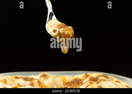 Makrofoto eines Dessertlöffels mit Karamell-Eis über einem Eisbehälter vor einem schwarzen Hintergrund mit Kopierfläche. Stockfoto
