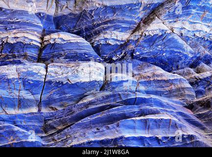 Fragment von rauer Oberfläche von schäbig blau lackierten felsigen Wand mit Kratzern und Rissen als texturierter Hintergrund Stockfoto