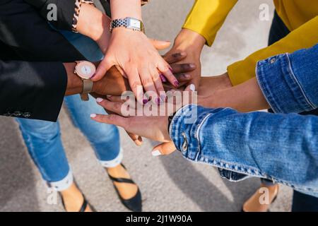 Von oben Gruppe von optimistischen Frauen Stapeln Hände zusammen mit Ernte gesichtslose Freunde, während auf der Straße gegen blauen Himmel stehen Stockfoto