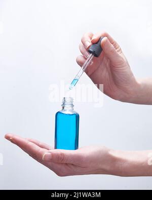 Hände von Ernte anonyme Person Tropfen blaue Hyaluronsäure aus der Pipette während der Hautpflege Routine in Licht Studio Stockfoto