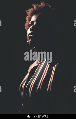Seitenansicht Silhouette der afroamerikanischen Frau mit krausem Haar in der Dunkelheit auf schwarzem Hintergrund stehen Stockfoto