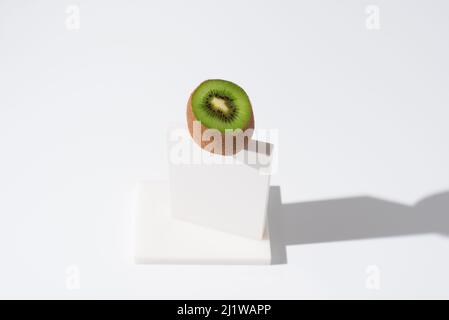 Schneiden Sie ungeschälte frische Kiwi auf weißem Ständer auf dem Tisch vor grauem Hintergrund im hellen Studio platziert Stockfoto