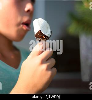 Essen Sie Eis. Eskimo in Schokolade auf einem Stock. Verschwommenes Gesicht eines Jungen. Stockfoto