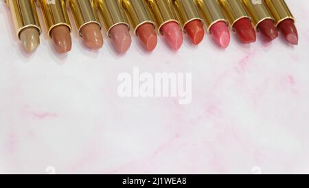 Lippenstifte in verschiedenen Rottönen, nebeneinander auf einem rosa Marmorgrund aufgereiht. Mit Kopierplatz im unteren Teil. Stockfoto