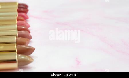 Lippenstifte in verschiedenen Rottönen, nebeneinander auf einem rosa Marmorgrund aufgereiht. Mit Kopierplatz auf der rechten Seite. Stockfoto