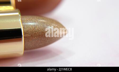 Nahaufnahme eines Tubus Lippenstift in Gold, auf einer rosa Oberfläche. Mit Kopierplatz auf der rechten Seite. Stockfoto