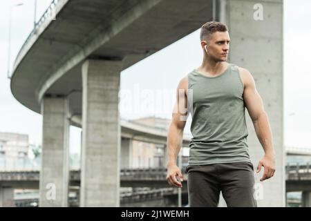 Schöner Mann mit einem wirlosen Ohrhörer. Musik hören während eines Fitnesstrainings auf der Straße. Stockfoto