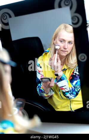 Eine attraktive, nachdenkliche Frau mittleren Alters sitzt am Spiegel und pudert ihr Gesicht mit einer Puderbürste Stockfoto