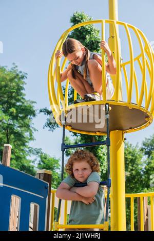 Junge auf einer Seilleiter, der die Kamera in der Nähe der Schwester auf dem hohen Turm im Vergnügungspark ansah Stockfoto